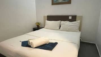 Una cama bien hecha con una toalla azul y otra enrollada, una mesita de noche con una pequeña planta, y un cuadro de una playa en la pared.