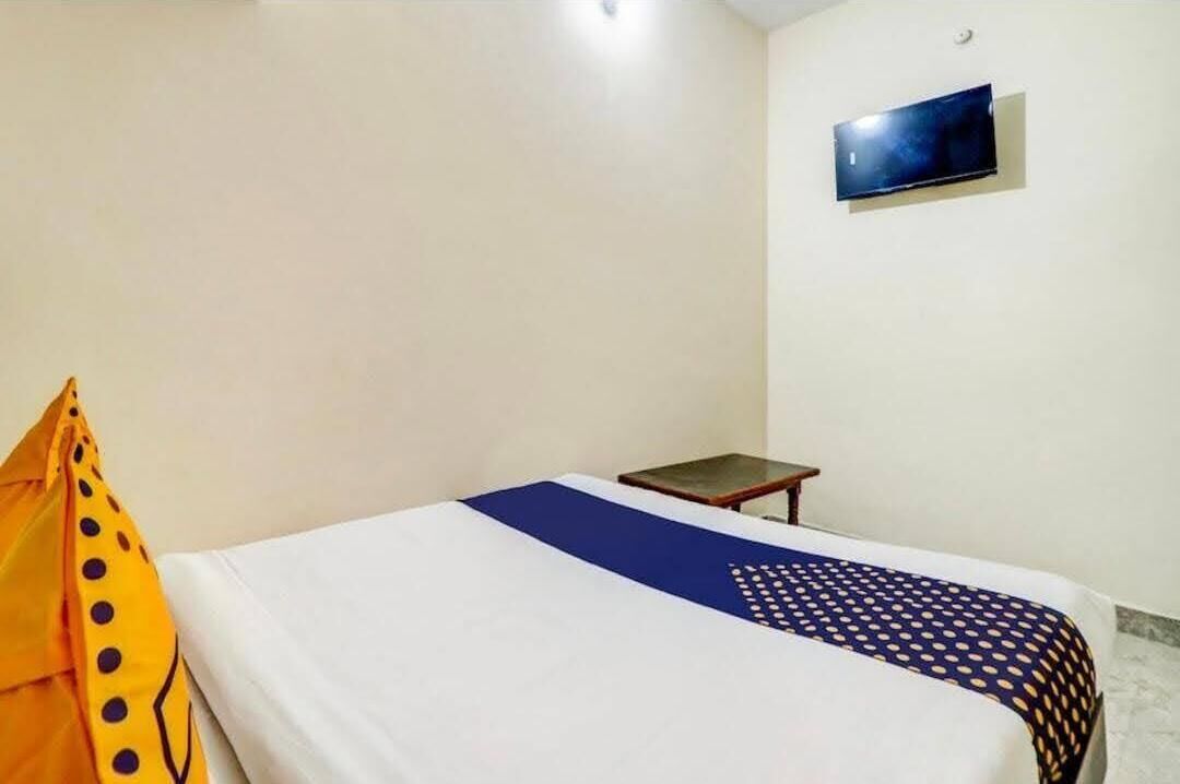 A single bed with a white and blue bedspread, a small bedside table, and a TV mounted on the wall.