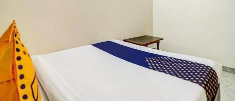 A single bed with a white and blue bedspread, a small bedside table, and a TV mounted on the wall.