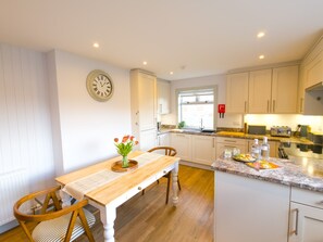 A kitchen with white cabinets, a wooden dining table, and a clock on the wall. - Lynemore Croft - rural cairngorm national park (Grantown-on-Spey)