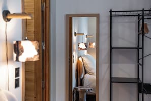 Ein Zimmer mit Holztür, einem Bett mit Kopfteil, einem Wandregal und einer Pendelleuchte.
