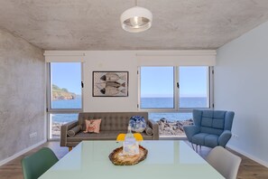 A modern living room with a large table, two sofas, a blue armchair, and a view of the sea through large windows. - GuestReady - Pepper of the Sea (Lagoa)