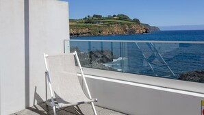 Ein Balkon mit freiem Blick auf das Meer und einen grasbewachsenen Hügel im Hintergrund.
