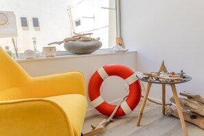 A yellow chair, a red and white life preserver, and a small table with driftwood and a bowl.