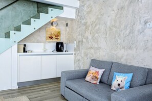 A modern living space with a grey sofa, a staircase, and a kitchen area.