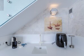 A modern kitchen with a coffee machine, kettle, and a painting of boats. - GuestReady - Pepper of the Sea (Lagoa)