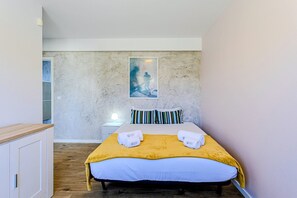 Ein Schlafzimmer mit einem Bett, einem Nachttisch, einer Lampe, einem Bild an der Wand und einem Holzboden.