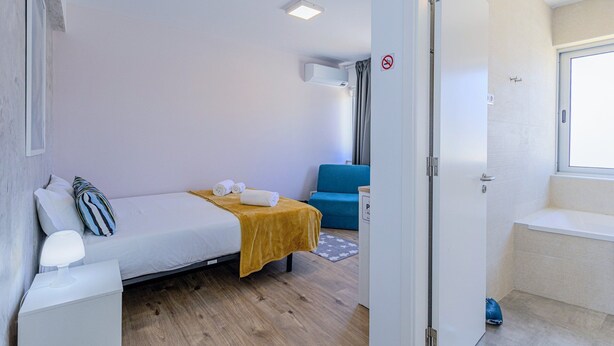 Ein Schlafzimmer mit einem Bett, einem Sessel, einem kleinen Tisch, einem Fenster und einer Tür.