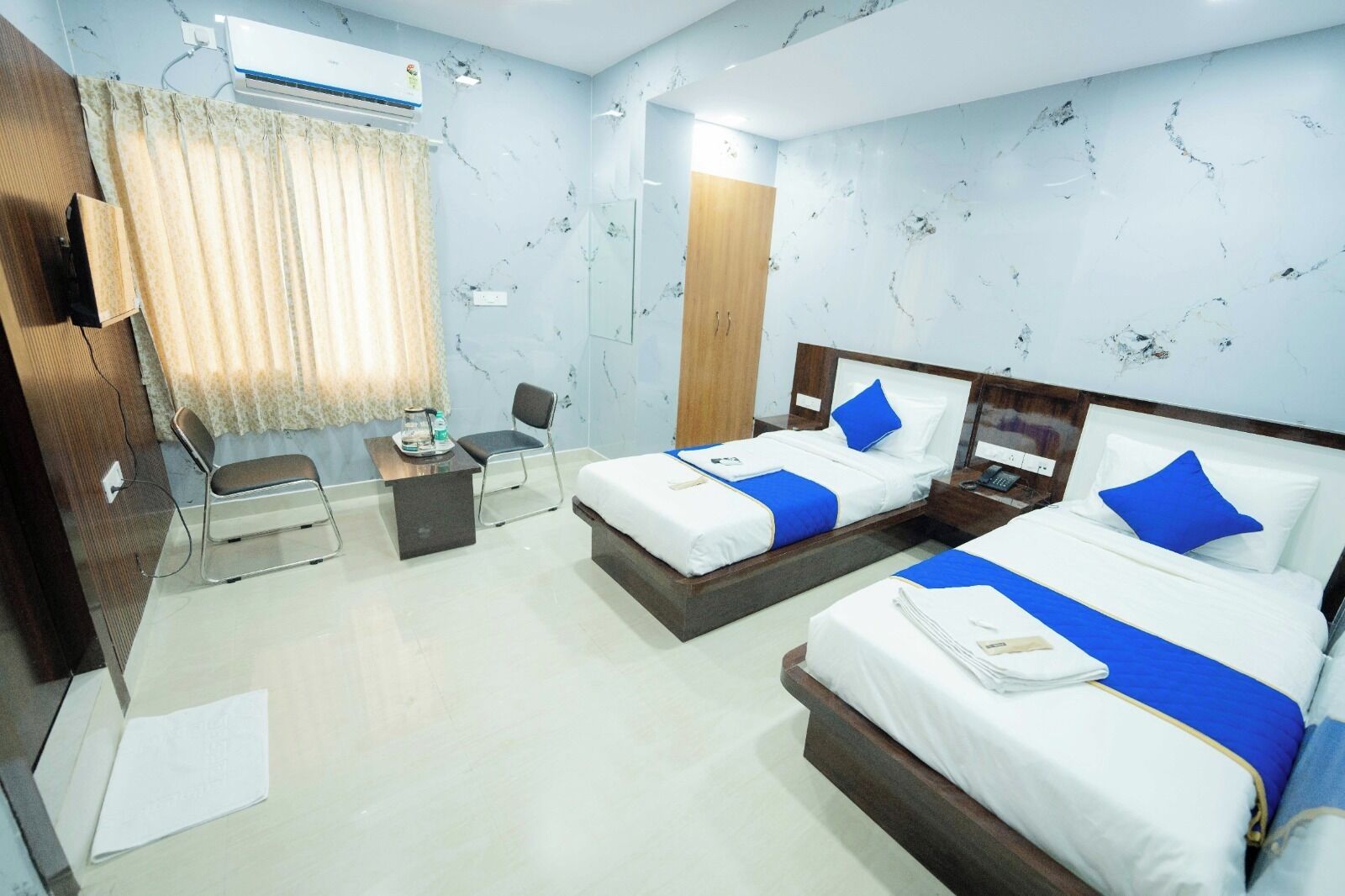 A hotel room with two beds, a desk, a chair, and an air conditioning unit.