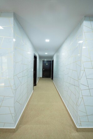 A hallway with white marble walls and a beige carpet. - Sri Sai Saara Inn (Bengaluru)