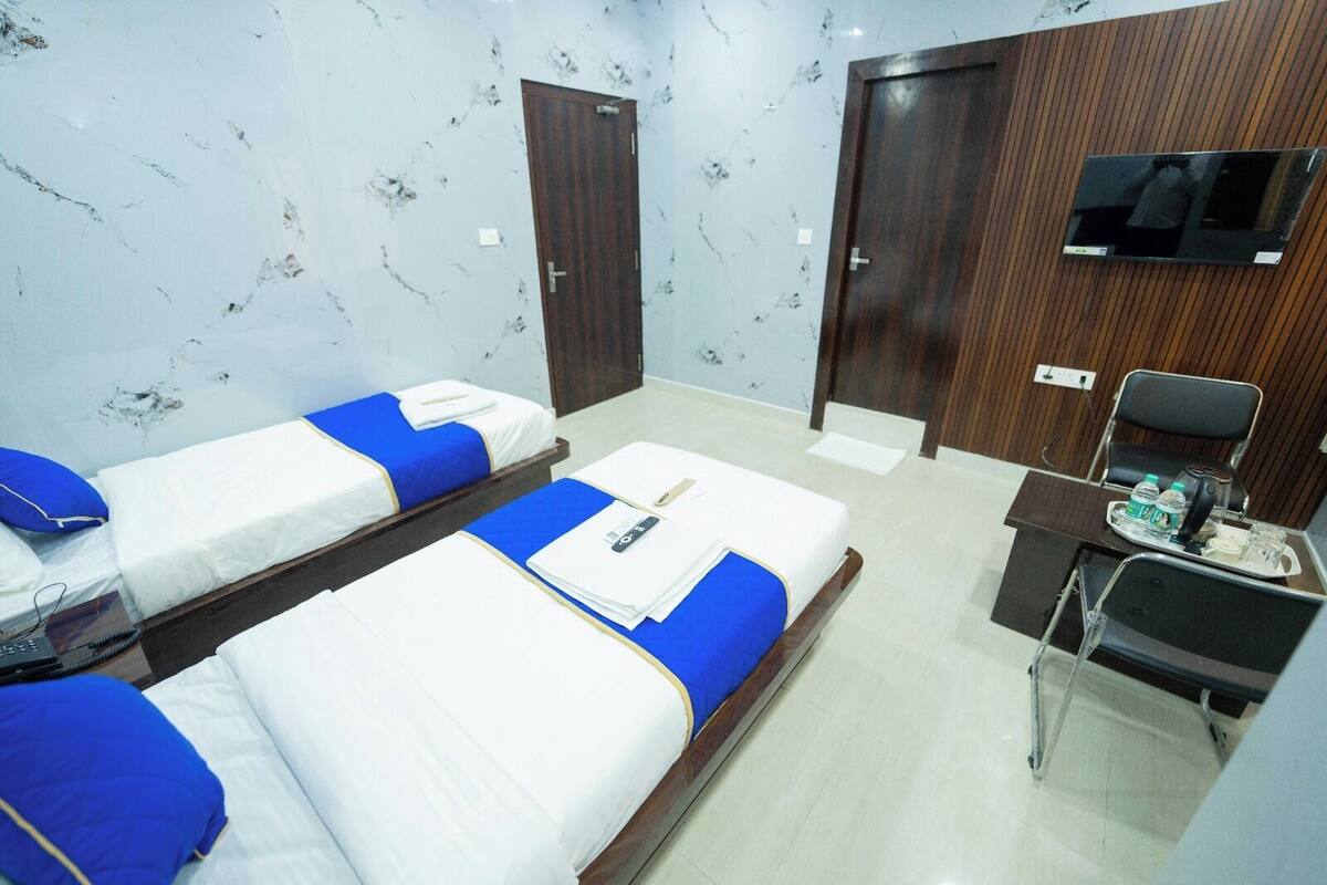 A hotel room with two single beds, a desk with a chair, a television, and a small table with water bottles.