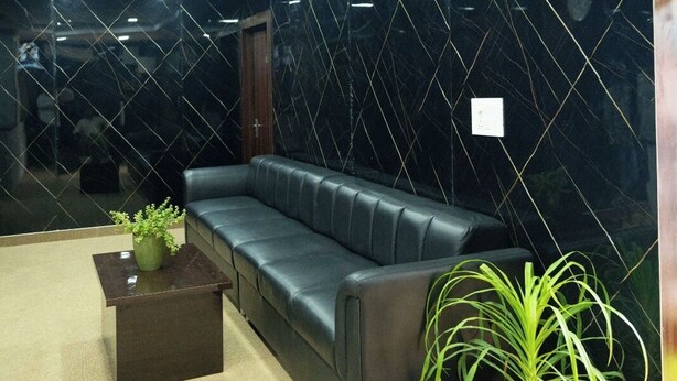 Un vestíbulo moderno con un sofá de cuero negro, una pequeña mesa con una planta y una pared de mármol.