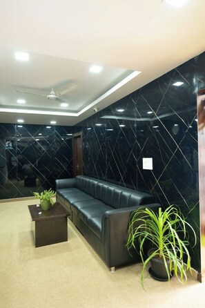 A modern lobby with a black leather sofa, a small table with a plant, and a marble wall. - Sri Sai Saara Inn (Bengaluru)