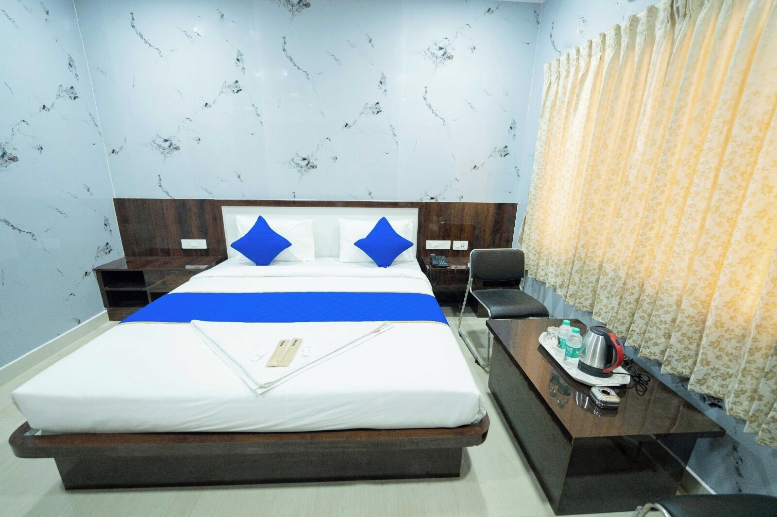 A hotel room with a bed, bedside tables, a desk, a chair, a telephone, and a curtain.