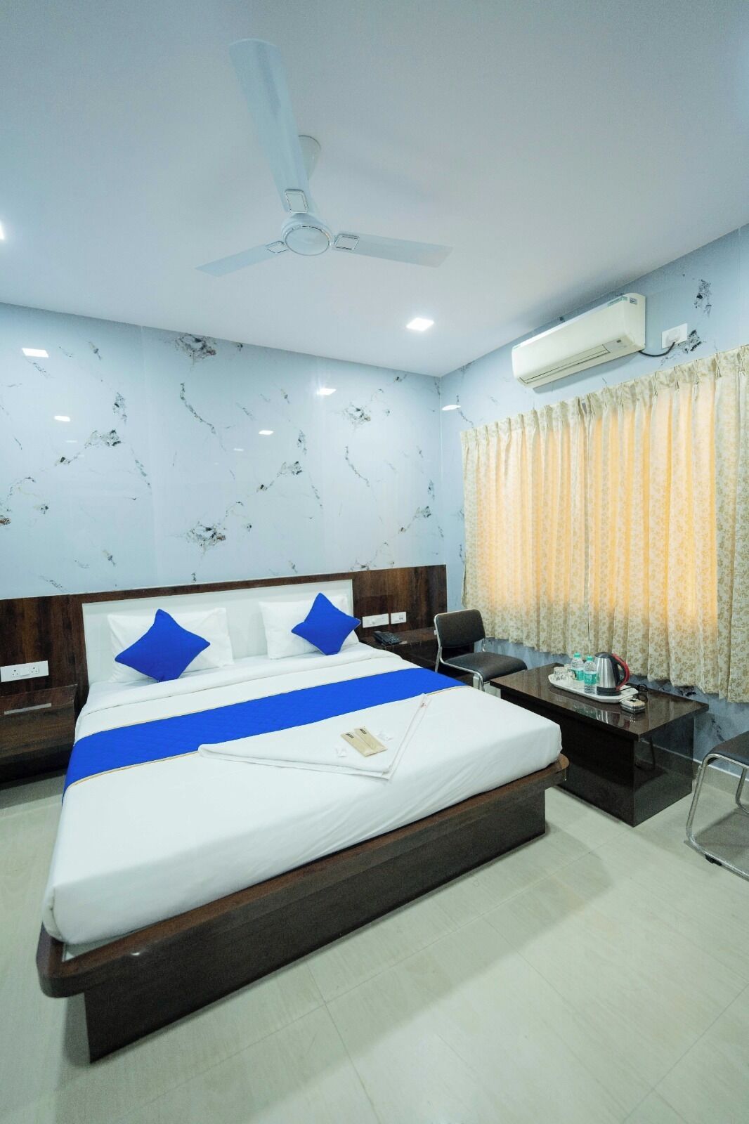 A hotel room with a bed, a desk, an air conditioner, and a ceiling fan.