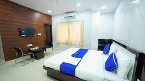 Una habitación de hotel con cama, escritorio, silla, televisor y aire acondicionado.