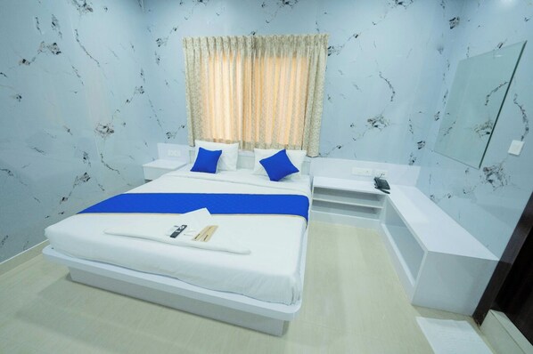 A hotel room with a large bed, bedside tables, a bedside lamp, a mirror, and a window with curtains. - Sri Sai Saara Inn (Bengaluru)