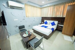 A hotel room with a bed, bedside table, chair, and an air conditioning unit. - Sri Sai Saara Inn (Bengaluru)
