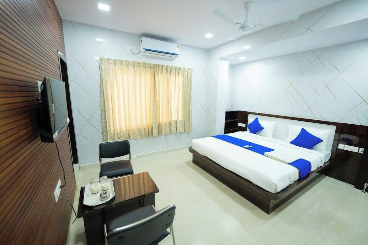 A hotel room with a bed, a desk, a chair, a television, and an air conditioning unit.