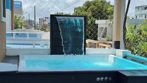 A hot tub with a waterfall feature, surrounded by a fence and buildings in the background. - The Duo by Suarez Properties | Jacuzzi & BBQ (Santo Domingo Este)