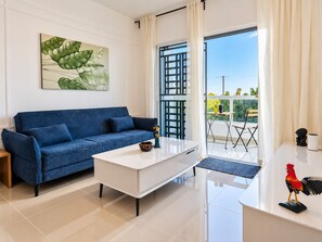 Un salon moderne avec un canapé bleu, une table basse blanche et un balcon offrant une vue agréable.