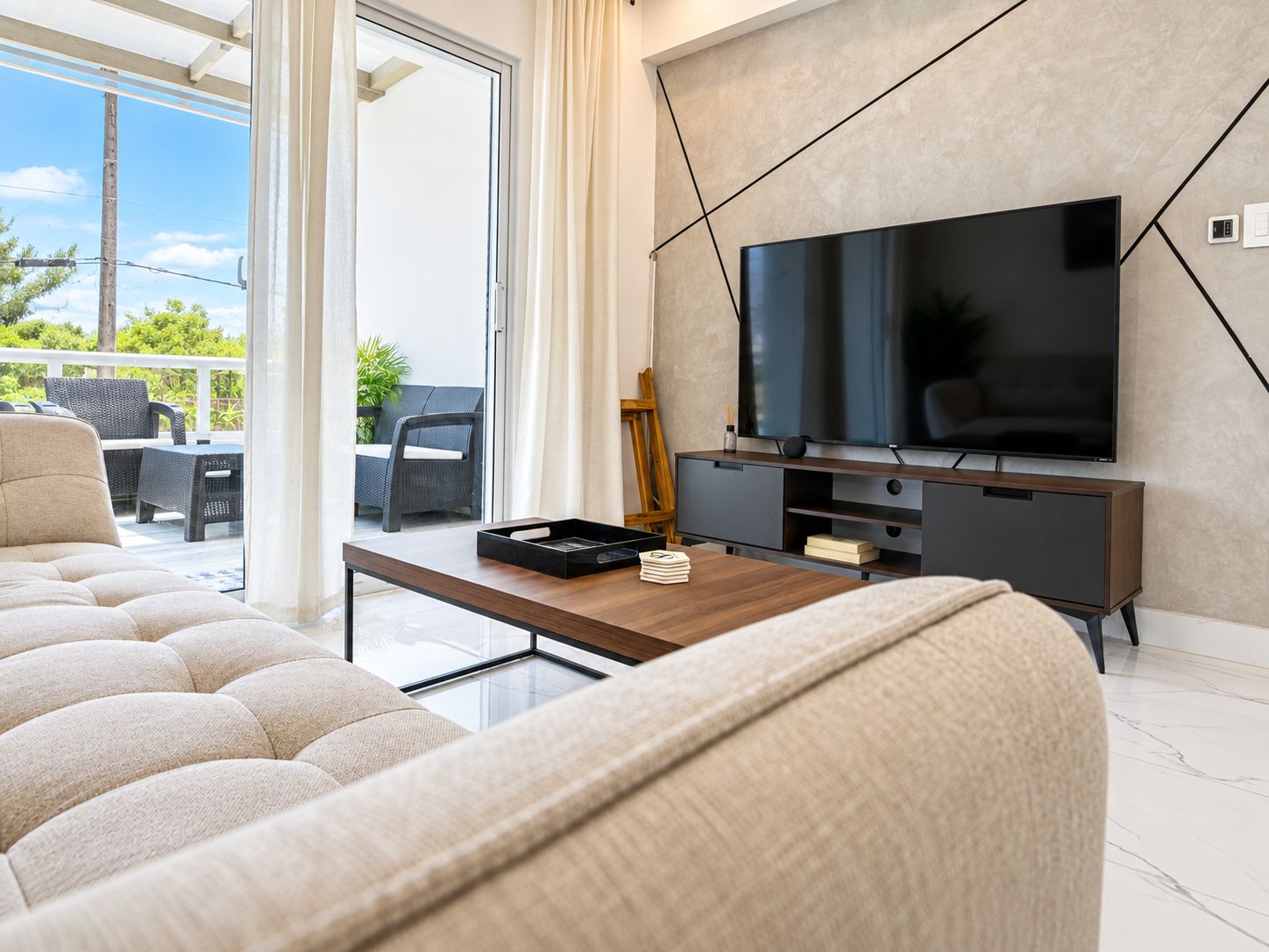 Una sala de estar moderna con un televisor de pantalla plana, un sofá, una mesa de centro y un ventanal corredero que da a un espacio exterior.