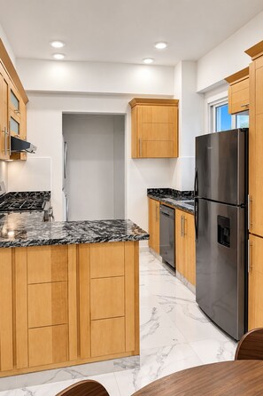 A modern kitchen with wooden cabinets, a stainless steel refrigerator, and a marble countertop. - The Duo by Suarez Properties | Jacuzzi & BBQ (Santo Domingo Este)