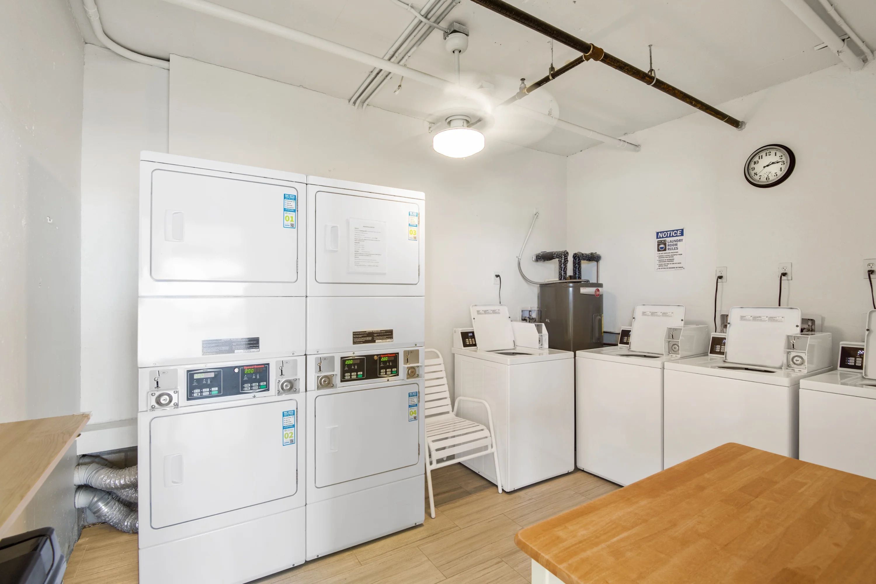 A laundry room with stacked washers and dryers, a coffee machine, and a clock on the wall.