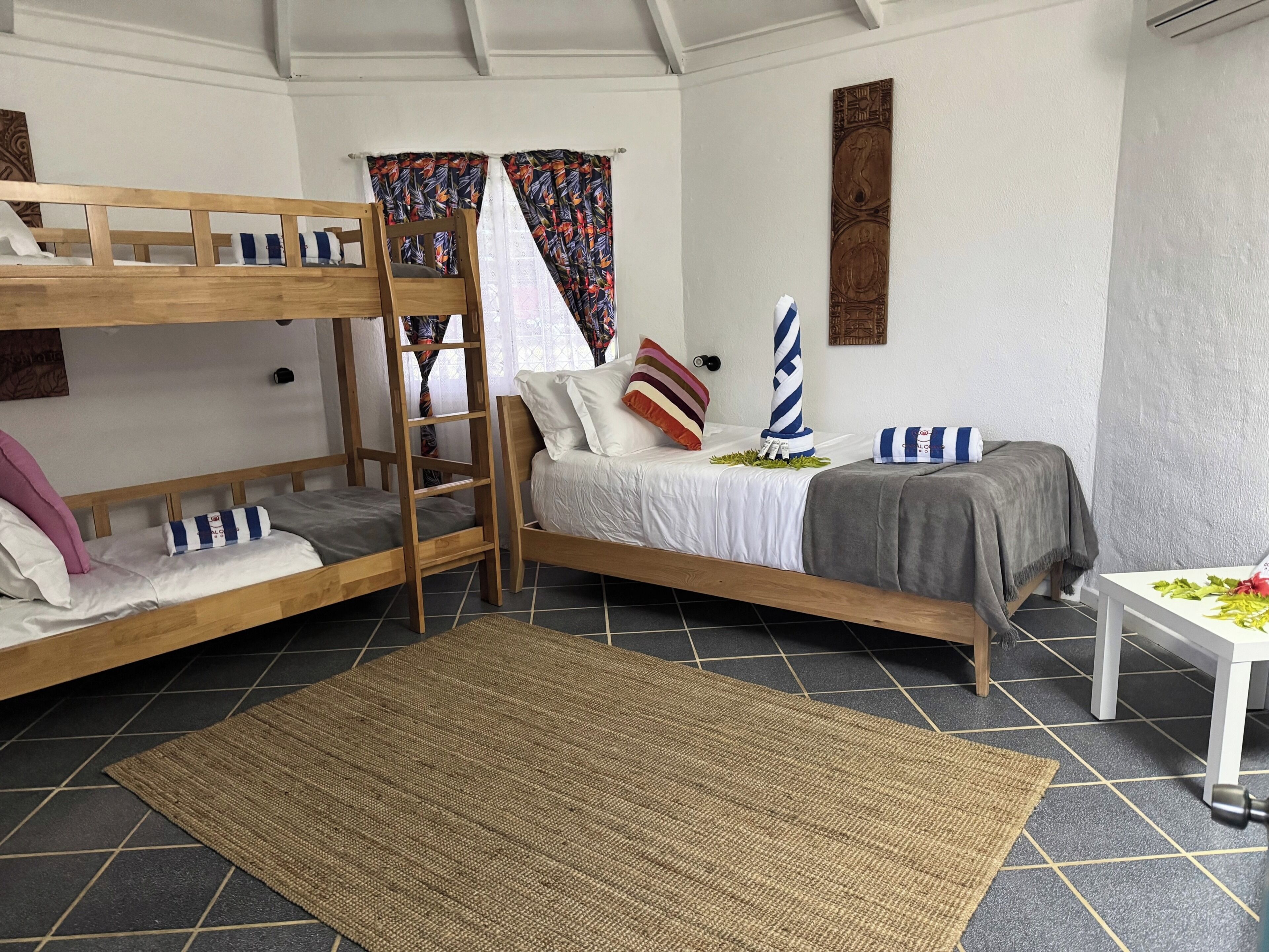 Una camera con un letto a castello, una scala, un letto singolo con cuscini, un tavolino con una pianta e un pannello decorativo sulla parete.