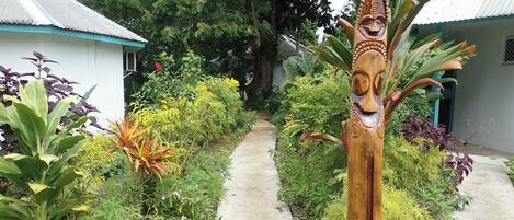 A pathway flanked by lush greenery and a wooden sculpture.