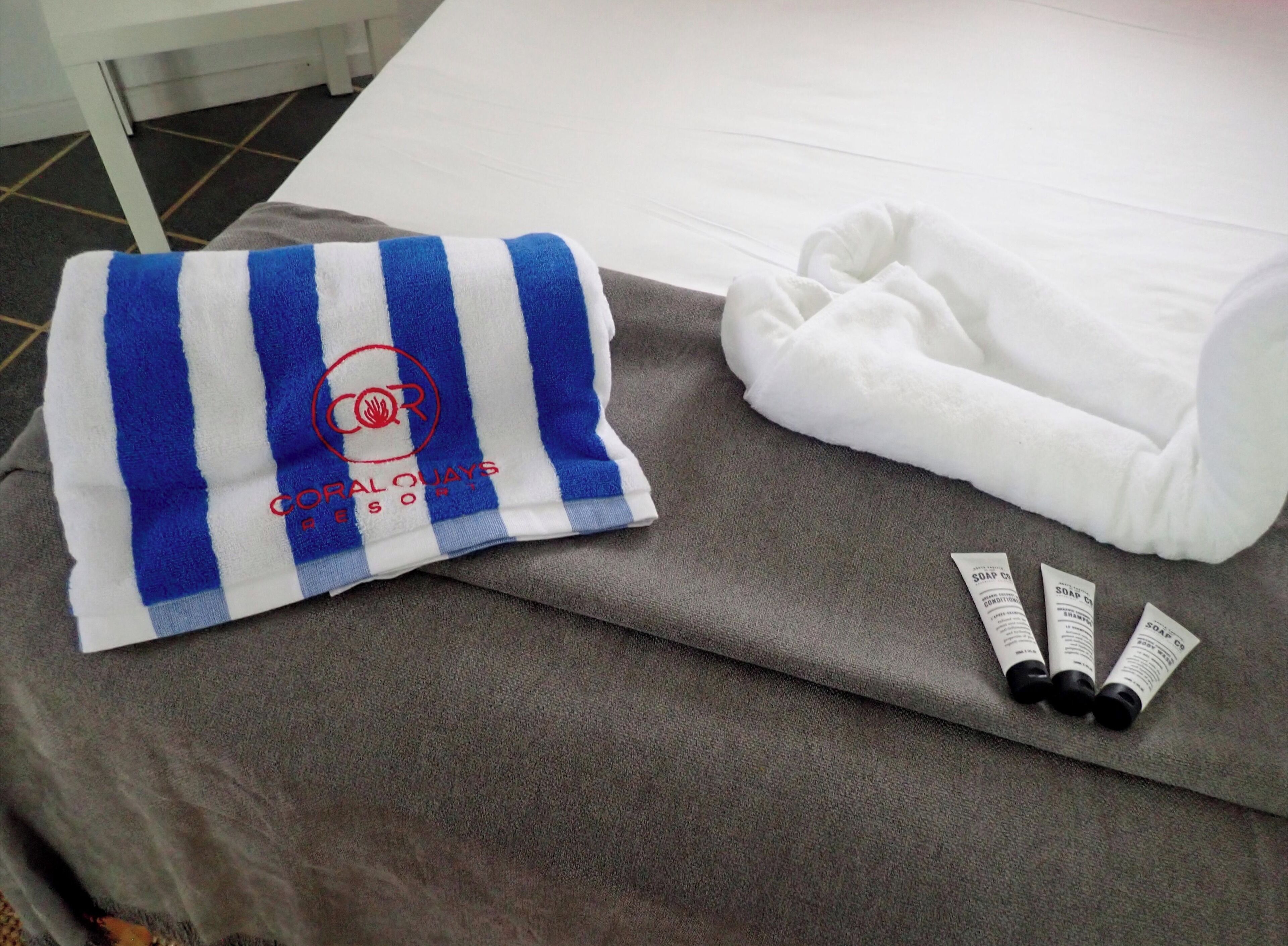 Una habitación de hotel con una toalla a rayas, una toalla blanca doblada y tres jabones sobre una superficie gris.