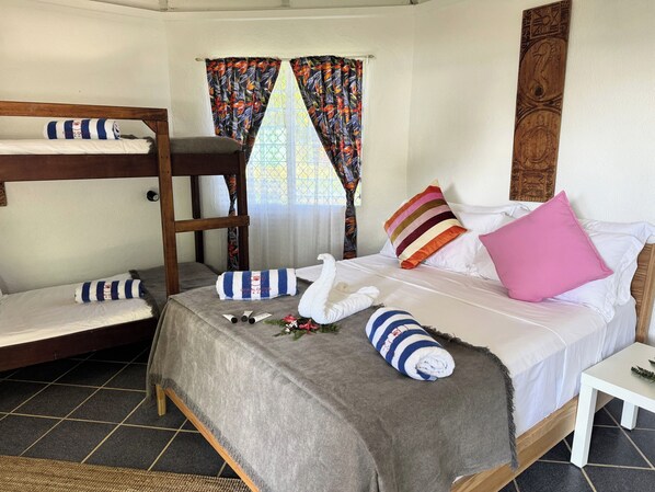 A room with a bunk bed, a single bed with pillows, a small table, and a window with curtains. - Coral Quays Resort (Luganville)