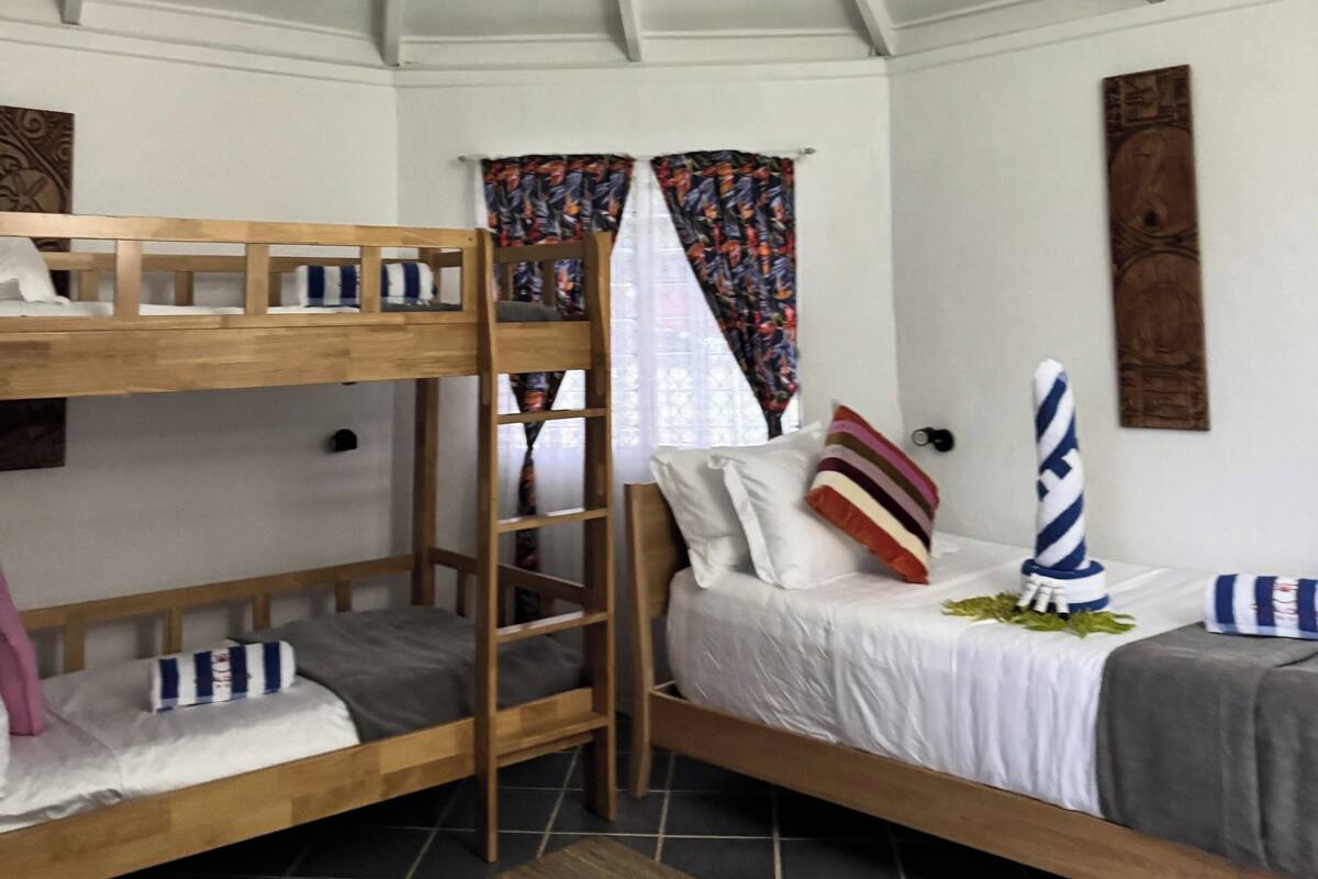 Et værelse med køjeseng, enkeltseng, ventilator og et vindue med mønstrede gardiner.
