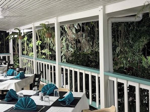 A restaurant with tables set for dining, a white ceiling, and a green railing.