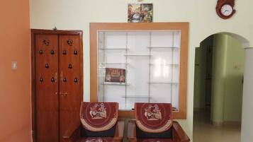 Une pièce comprenant deux chaises en bois, une armoire en bois, une fenêtre ornée d’un cadre décoratif et une horloge murale.