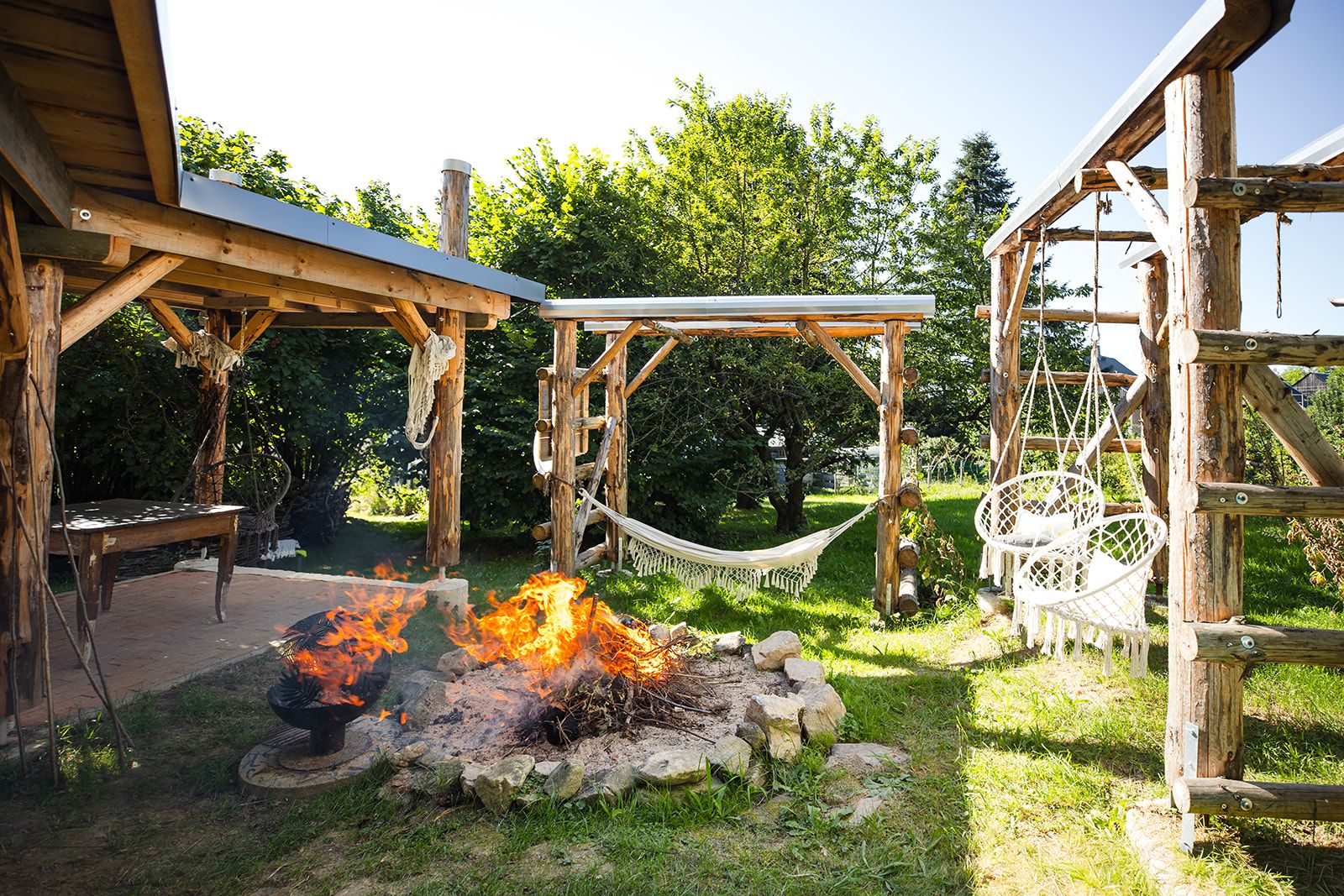 Une structure extérieure en bois comprenant un foyer, un hamac et une balançoire.