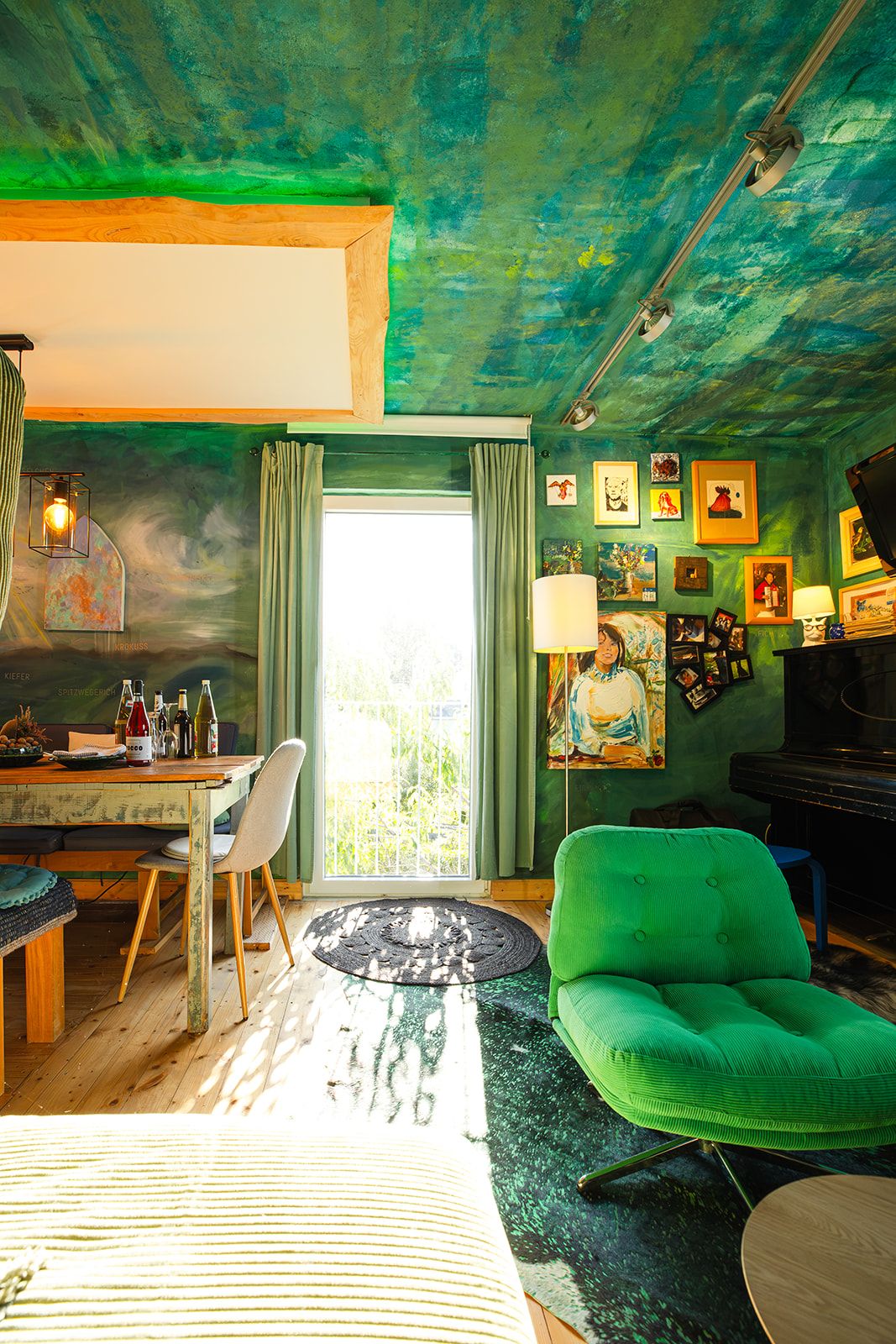 A room with a green chair, a dining table with chairs, a piano, and artwork on the walls.