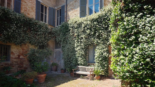 A courtyard with a brick pathway, a bench, potted plants, and a building with windows and shutters. - Dimora Castracane - House in historic building from 1400 with cloister, balcony and private parking space (Fano)
