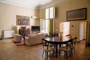 A spacious living area with a sofa, dining table, chairs, a television, and artwork on the walls.