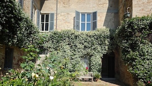 A courtyard with a cobblestone path, a bench, and a building with a brick facade and windows. - Dimora Castracane - House in historic building from 1400 with cloister, balcony and private parking space (Fano)