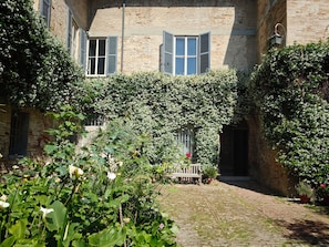 A courtyard with a cobblestone path, a bench, and a building with a brick facade and windows.