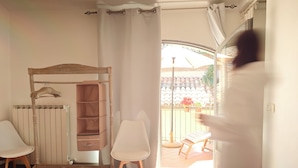 A room with a wooden bed, a white chair, a wooden wardrobe, and a view of an outdoor patio with a chair and potted plants. - Dimora Castracane - House in historic building from 1400 with cloister, balcony and private parking space (Fano)