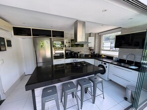 Uma cozinha moderna com uma ilha central, banquetas, máquina de lavar e uma janela grande.