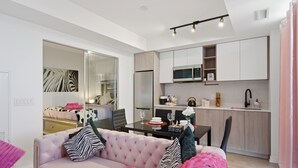 A modern living room with a pink sofa, a dining table, and a kitchen area with white cabinets and a microwave.