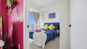 A bedroom with a bed, a bedside table, a wall-mounted plant, and a window with curtains.