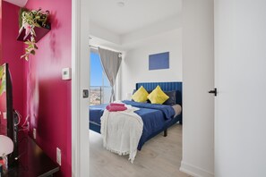 Une chambre à coucher avec un lit, une table de chevet, une plante fixée au mur et une fenêtre avec des rideaux.