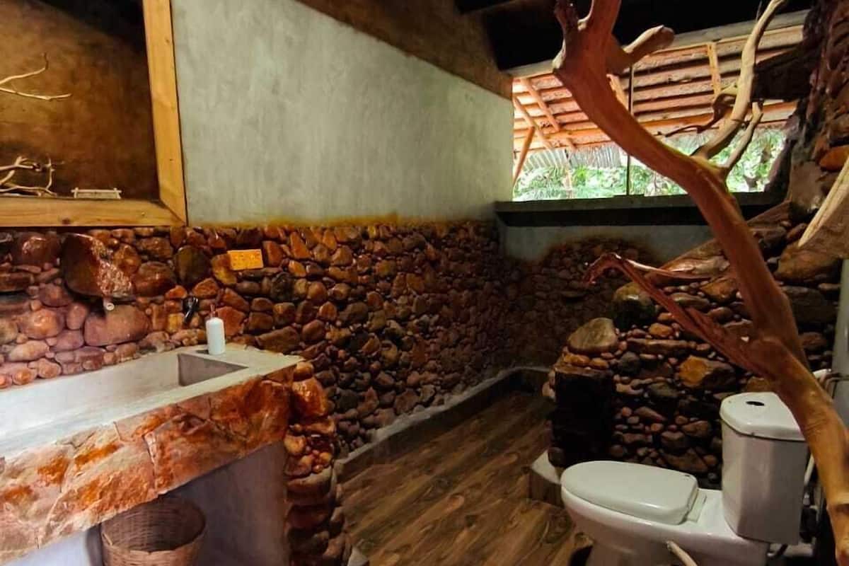 Un baño rústico con suelo de madera, pared de piedra, lavabo de madera y un inodoro.