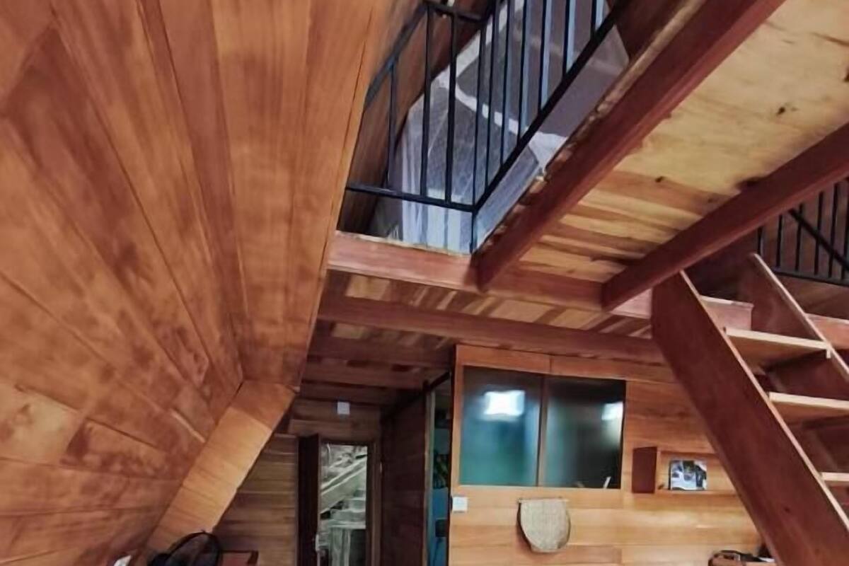 Un interior de madera con una cama, una escalera y vistas al exterior.