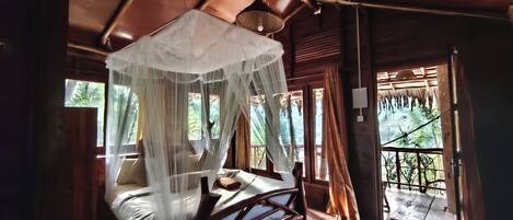Habitación de madera con cama bajo un dosel, ventanas amplias y balcón con vistas a zonas verdes.