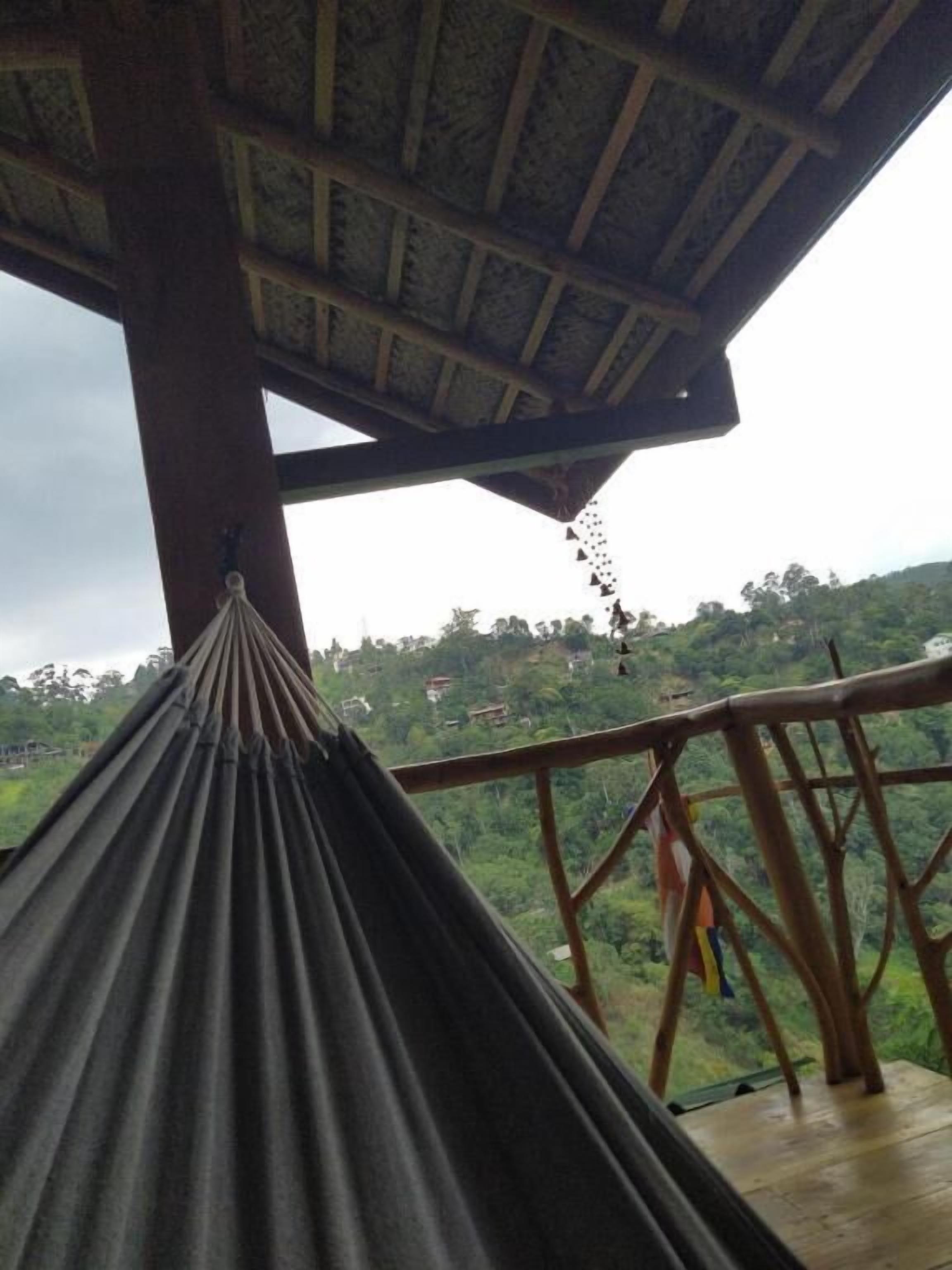 A hammock under a wooden structure with a view of a green landscape.